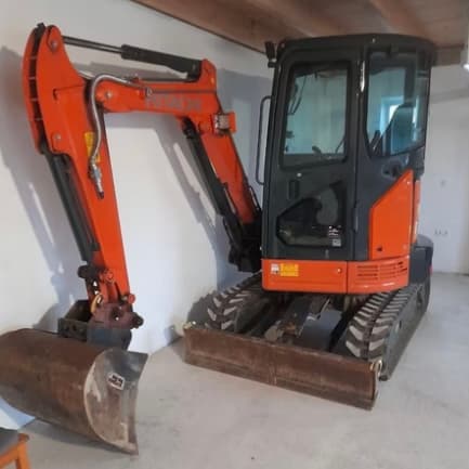 Oranger Bagger mit Fahrerkabine steht auf Betonboden.