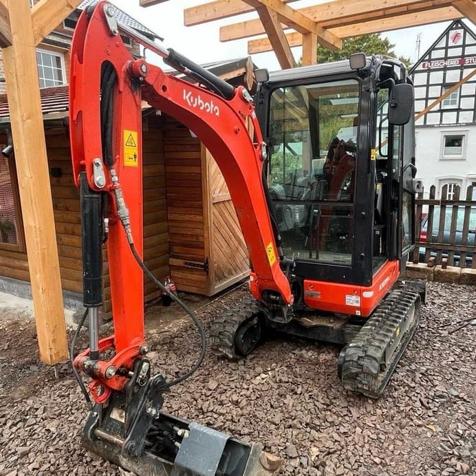 Oranger Bagger mit Fahrerkabine steht auf Betonboden.